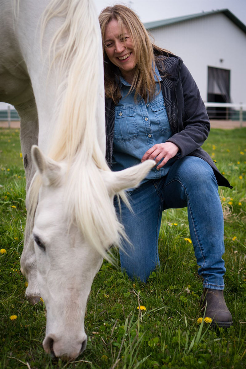 Lynn Thomas kneeling on one knee next to a white horse
