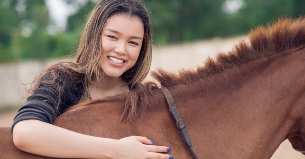 Young woman with arm around a horse's back