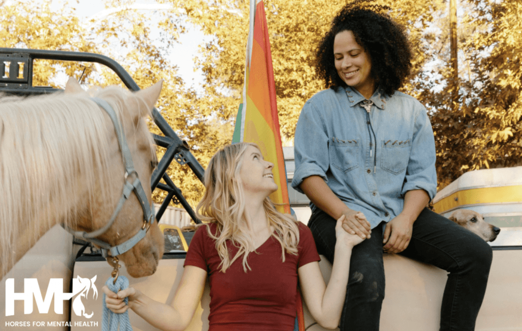 A couple holding hands with each other, while a horse stands beside them.